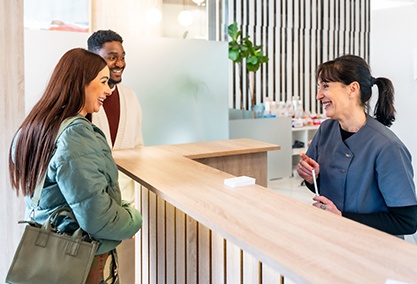 Dental receptionist smiling at couple in lobby