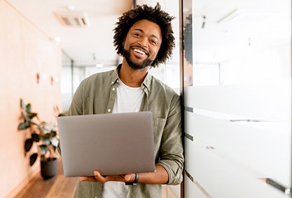 Man smiling while holding laptop in office