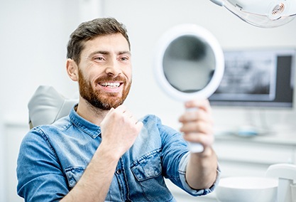 Man smiling at reflection in handheld mirror