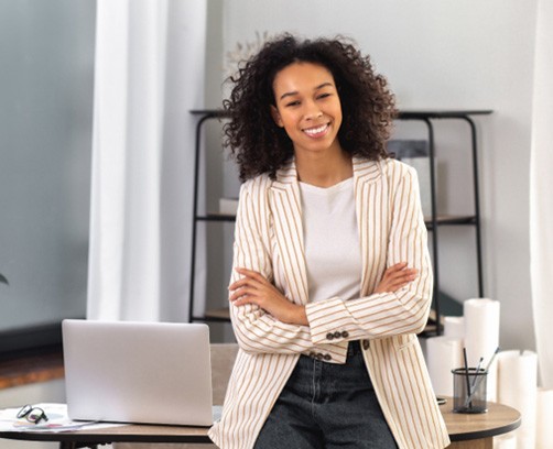 a business woman smiling and leaning against a desk